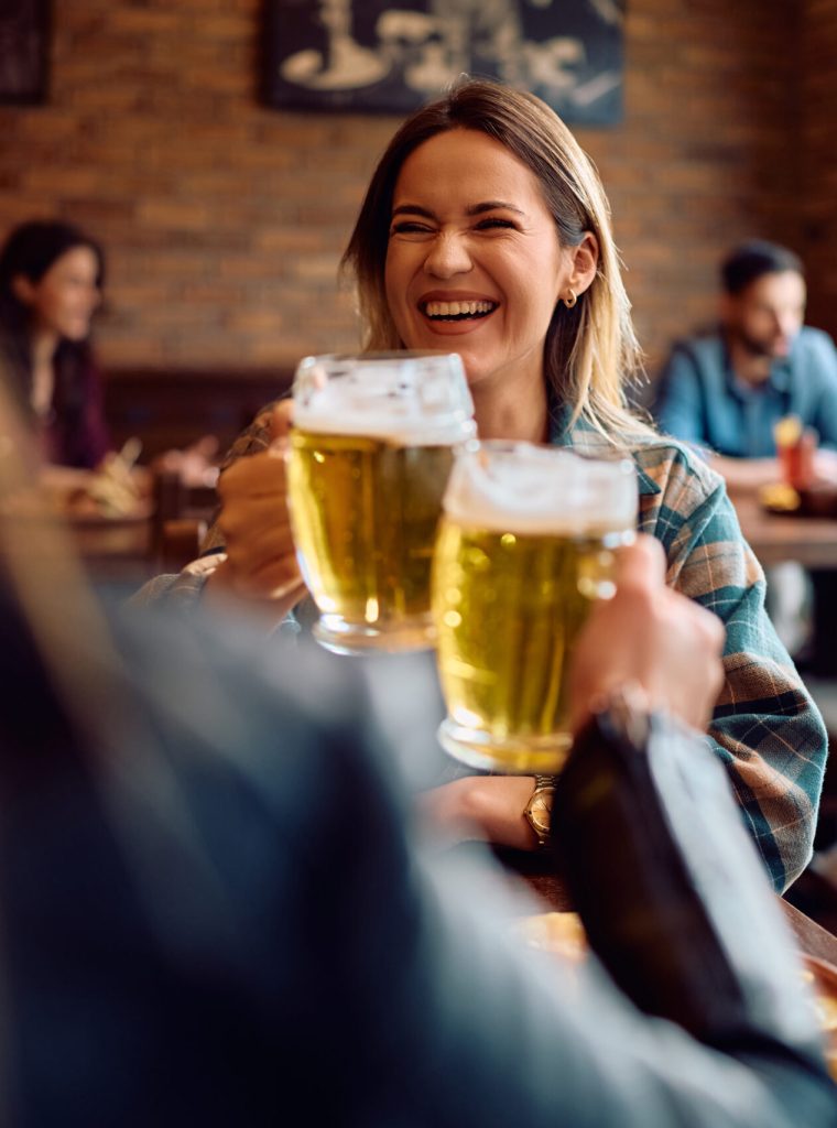 Happy woman and her female friends toasting with beer while gathering in a bar.